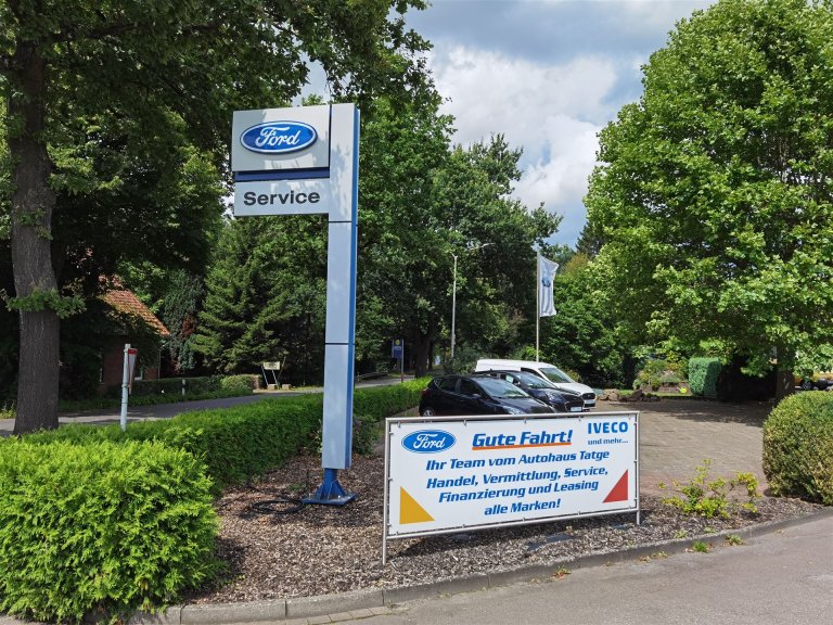 Eingangsschild mit Neuwagen daneben 